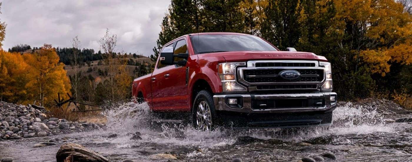 A red 2021 Ford F-250 driving through a shallow river.
