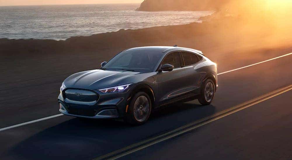 A gray 2021 Ford Mustang Mach-E is shown driving near an ocean.