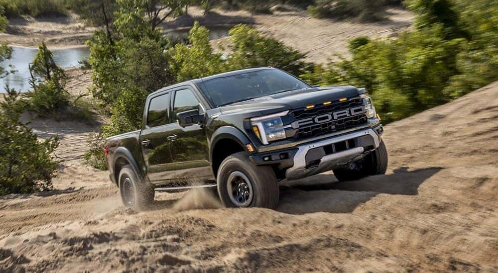 A black 2024 Ford F-150 Raptor is shown driving uphill.