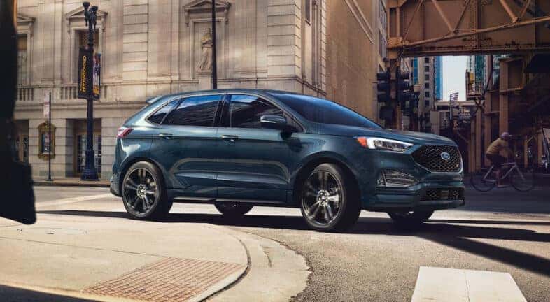 A blue 2024 Ford Edge ST turning the corner on a city street.