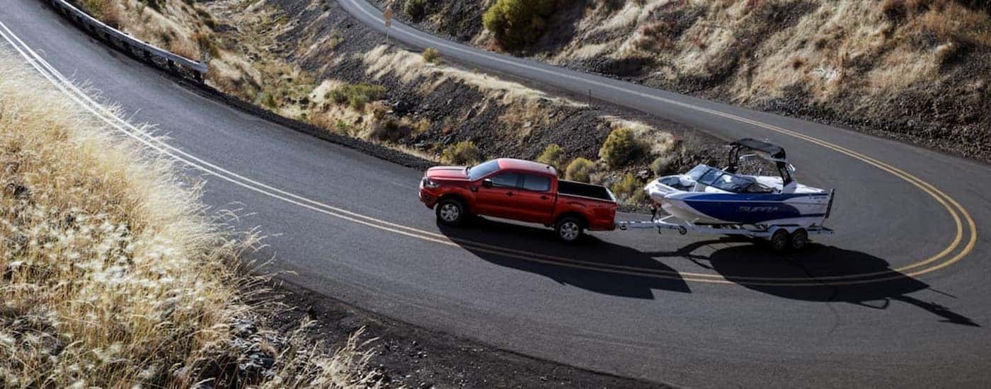 A red 2020 Ford Ranger is towing a boat on a winding road.