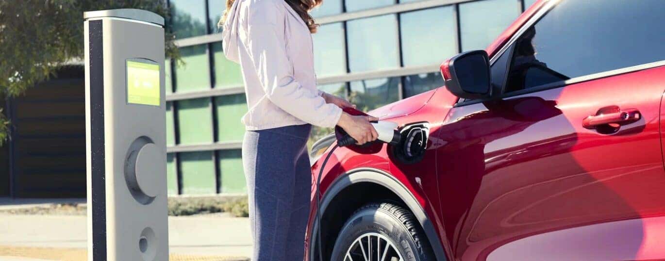 A woman charging a red 2025 Ford Escape PHEV at a public charging station.