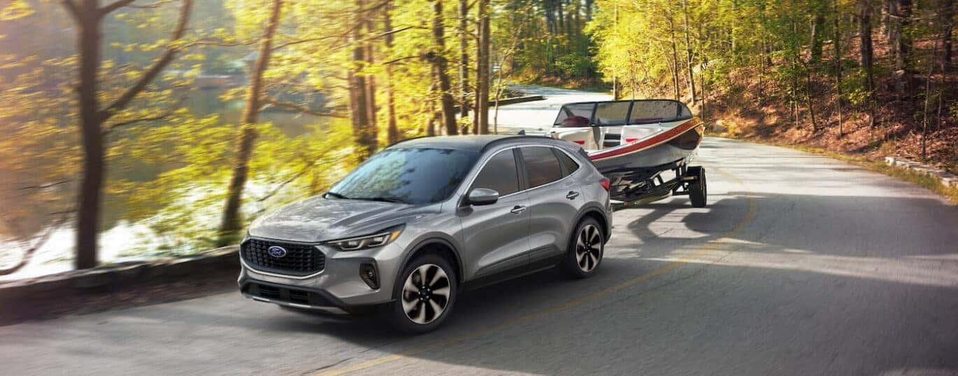 A silver 2025 Ford Escape Platinum towing a boat past water.