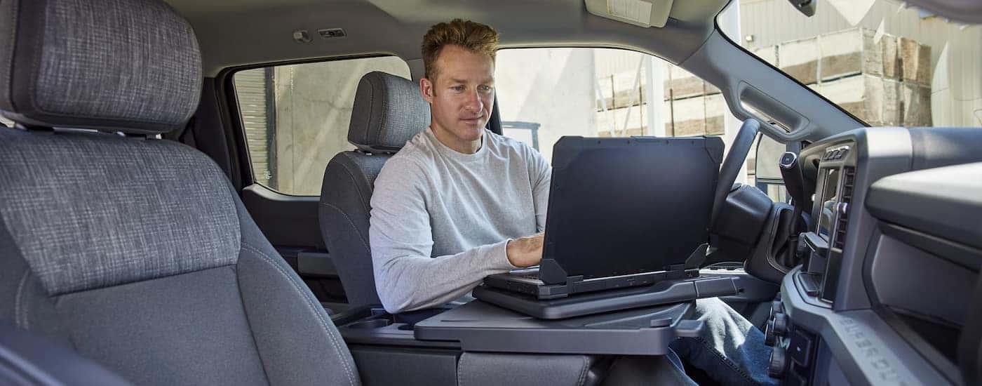 A man working on a laptop in the cab of a 2024 Ford F-350 for sale.