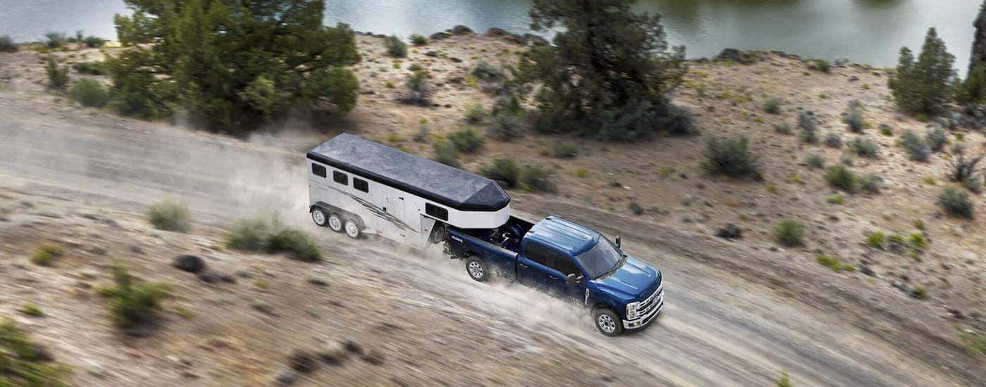 Overhead view of a blue 2024 Ford F-350 XLT towing a trailer on a dusty road.