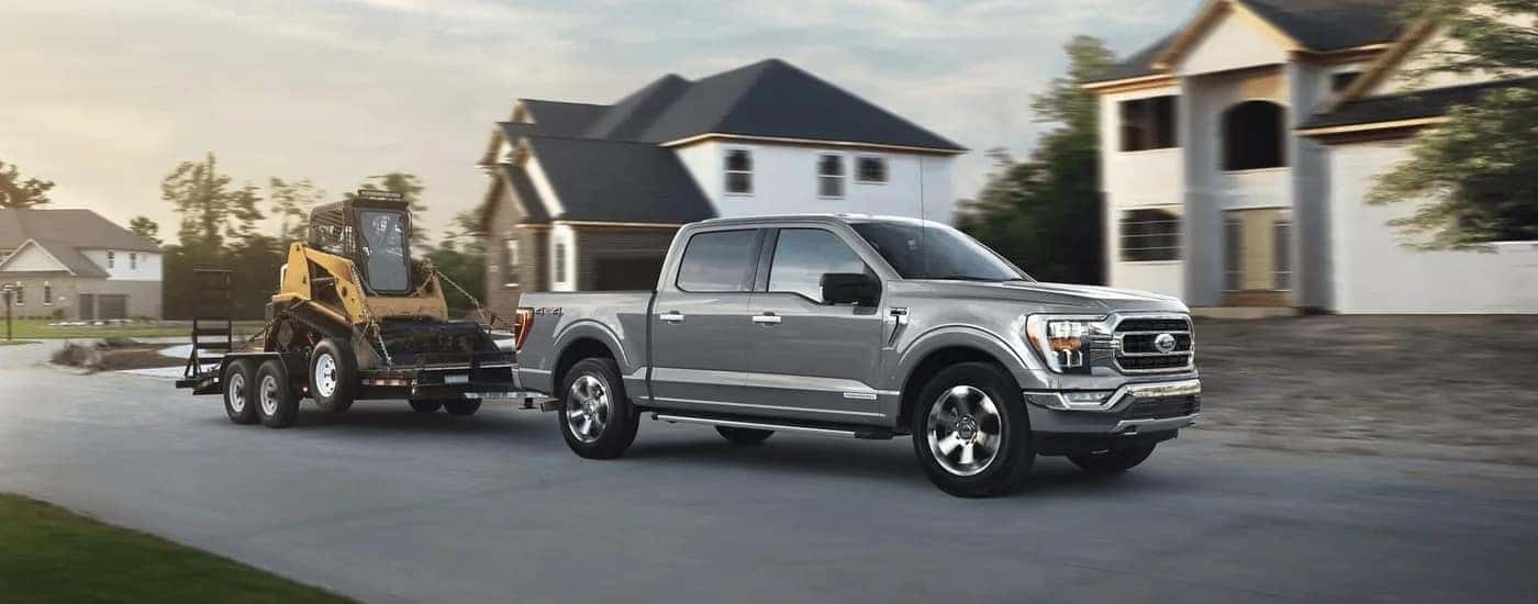 A silver 2023 Ford F-150 is shown from the side while towing a skidsteer.