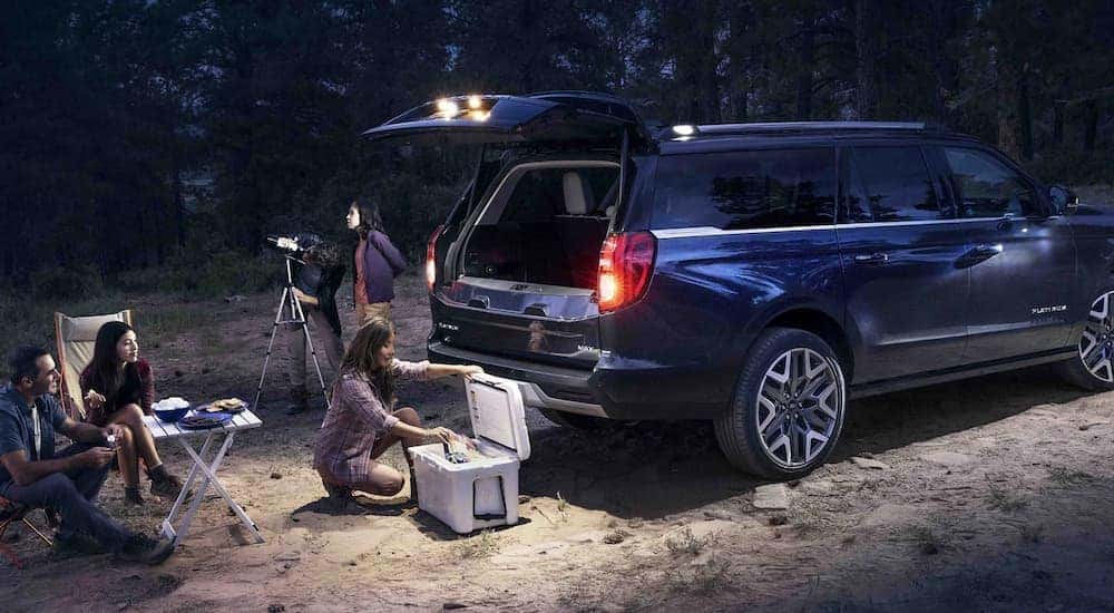 Rear view of people resting near a blue 2025 Ford Expedition Platinum with an open hatchback.