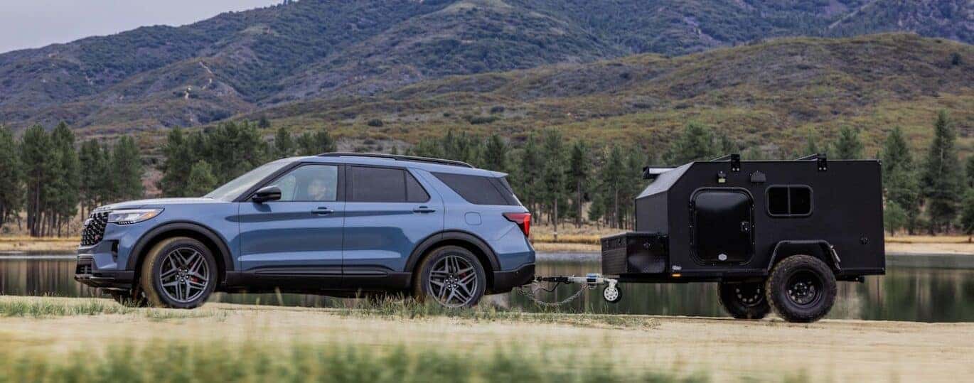 A blue 2025 Ford Explorer ST-Line is shown towing a trailer off-road.