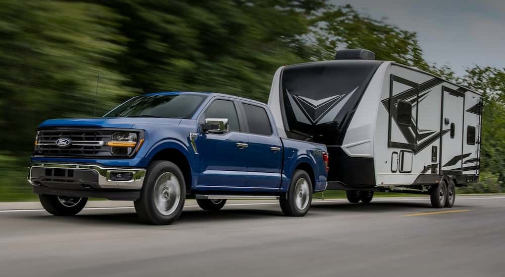 A blue 2025 Ford F-150 FX4 is shown towing a trailer on a highway.