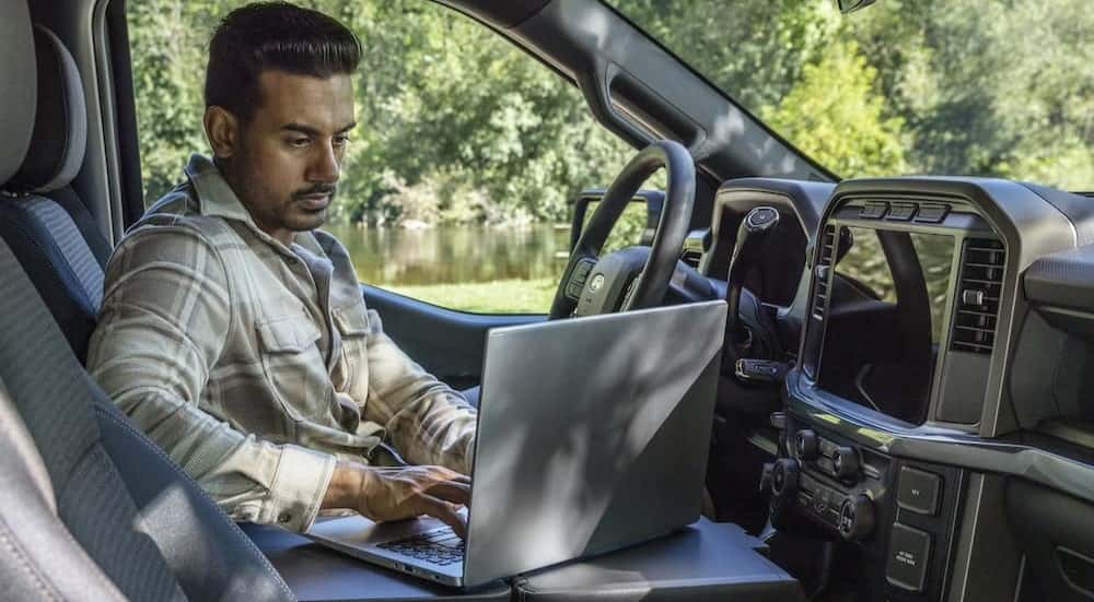 A person is shown using a laptop in a 2025 Ford F-150 for sale in Albany.
