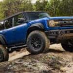 A blue 2025 Ford Bronco Raptor off-roading over boulders.