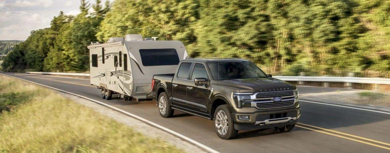 A gray 2025 Ford F-150 Platinum Plus is shown towing a trailer.