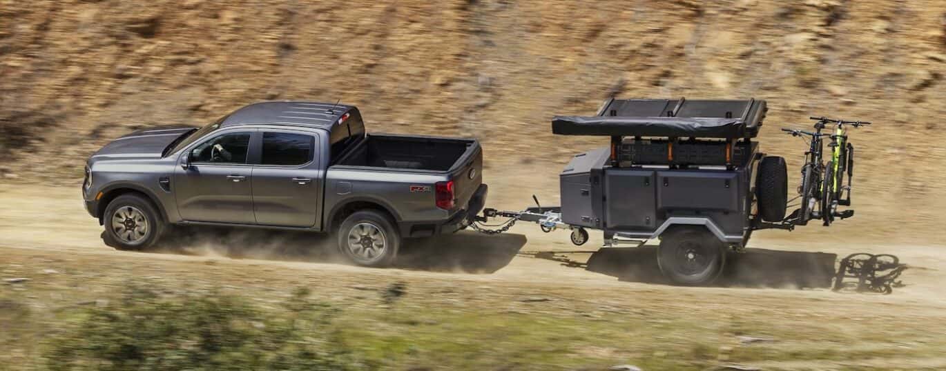 A silver 2025 Ford Ranger FX4 is shown towing a trailer off-road.