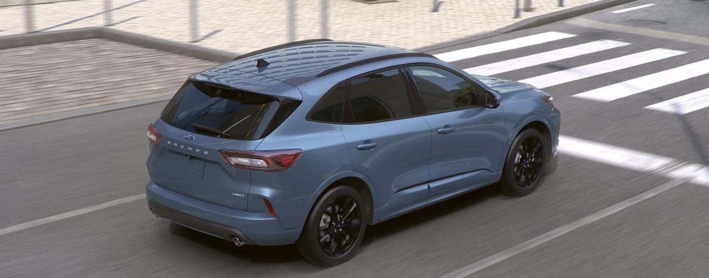 Rear overhead view of a pale blue 2024 Ford Escape ST-Line Elite driving through a city.