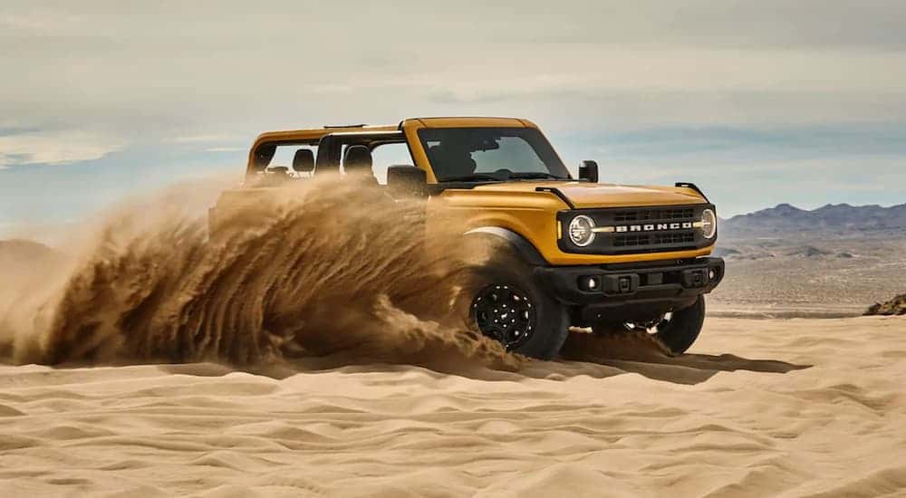 A yellow 2024 Ford Bronco kicking up sand while off-roading in a desert.