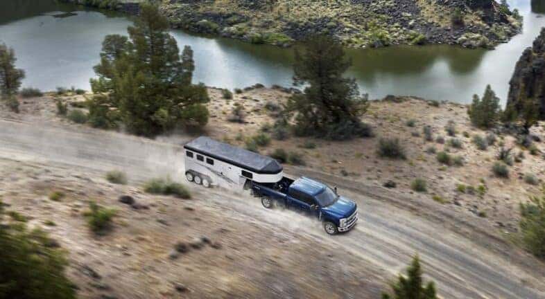 A blue 2023 Ford F-250 Super Duty is shown driving on a dirt road