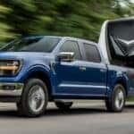 A blue 2025 Ford F-150 XLT towing a trailer.