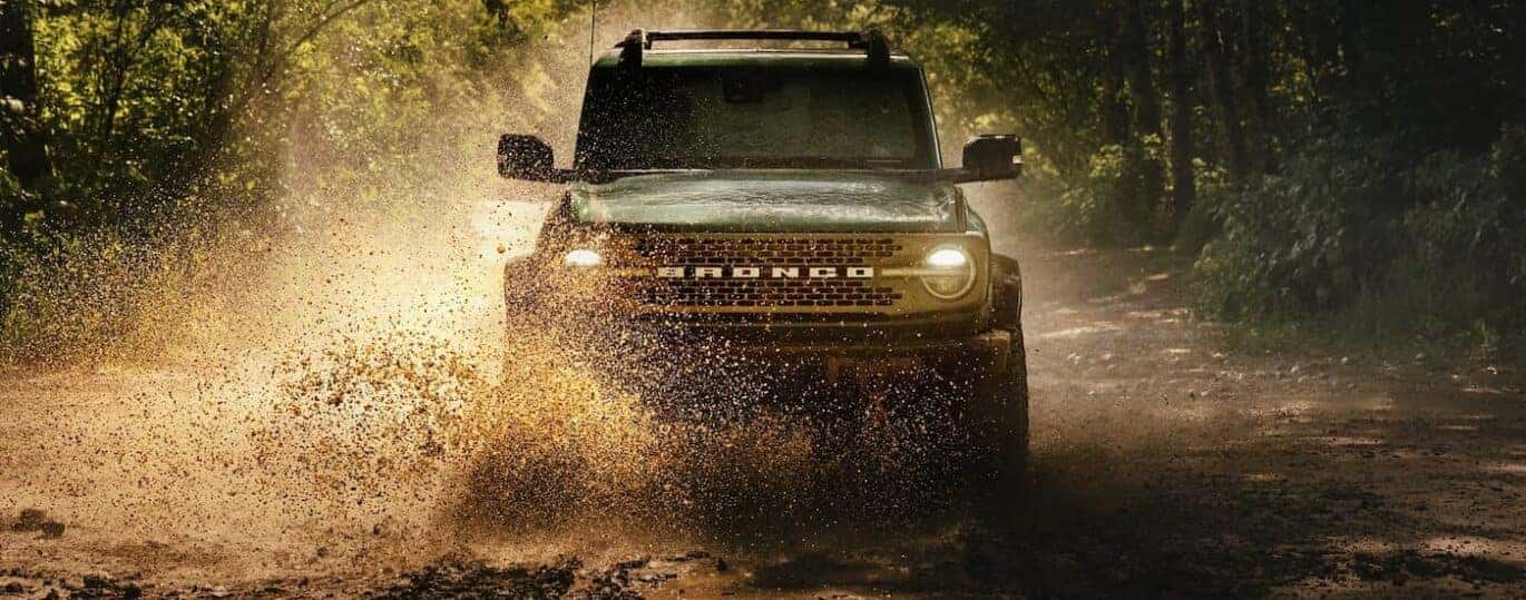 A green 2025 Ford Bronco Badlands is shown driving on muddy terrain.