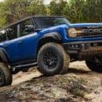 A blue 2025 Ford Bronco Raptor off-roading during a 2025 Ford Bronco vs 2025 Jeep Wrangler comparison.