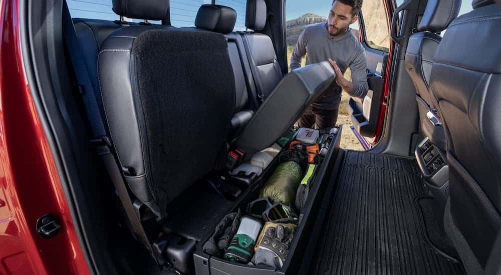 A man retrieving cargo from under the seats in a red 2025 Ford F-150 XLT.