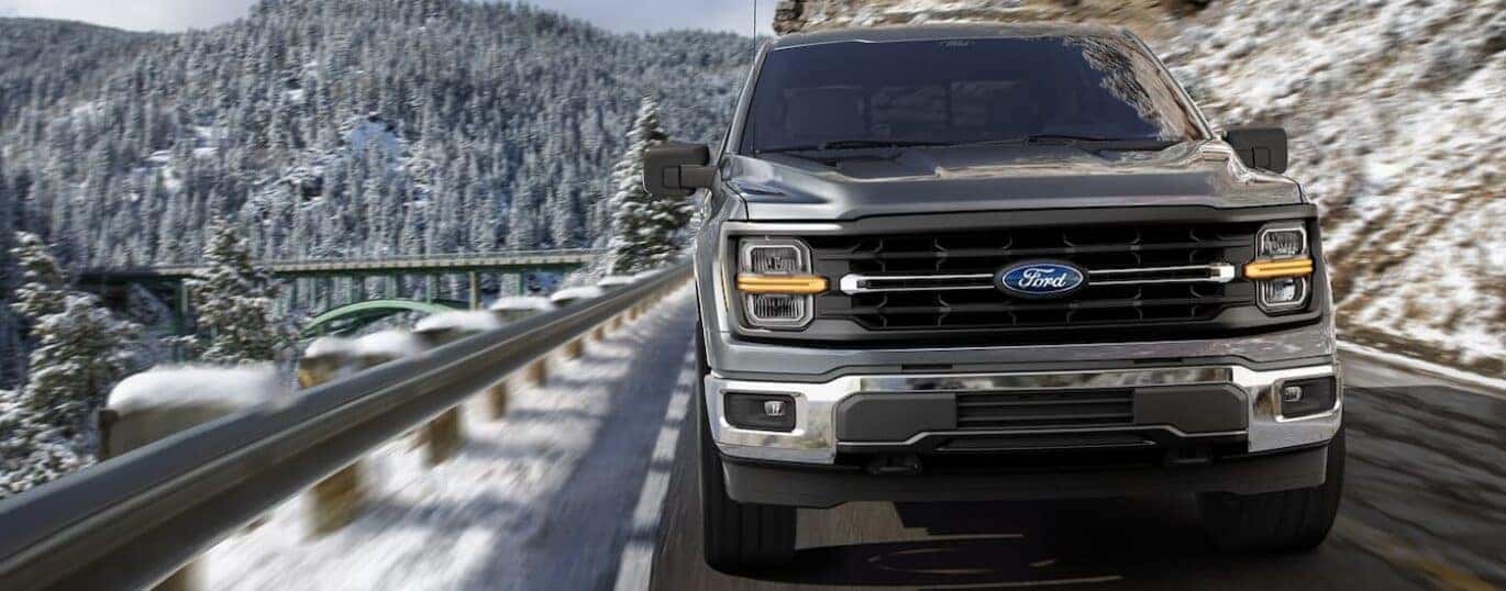 A grey 2025 Ford F-150 XLT driving on a snowy mountain road.