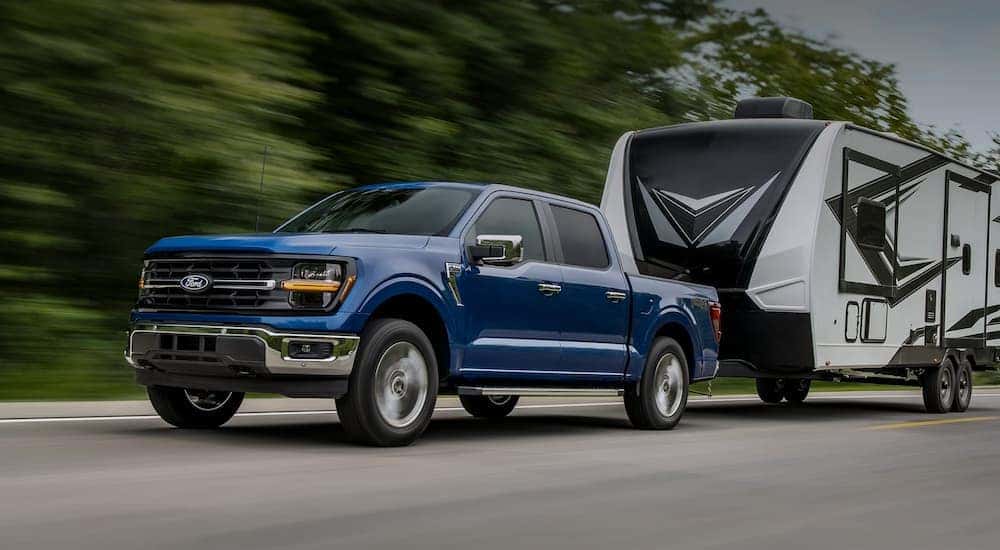 A blue 2025 Ford F-150 towing a camper.