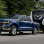 A blue 2025 Ford F-150 towing a camper down a road.