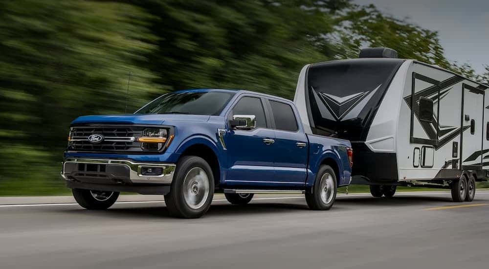 A blue 2025 Ford F-150 towing a camper down a road.