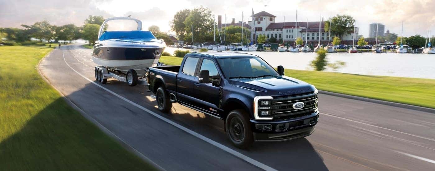 A black 2025 Ford F-350 Platinum is towing a boat past a marina.