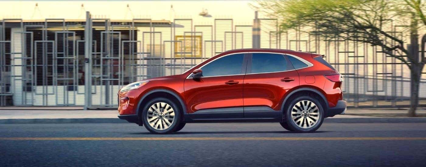 Side angle view of a red 2020 Ford Escape for sale near Troy driving down a road.