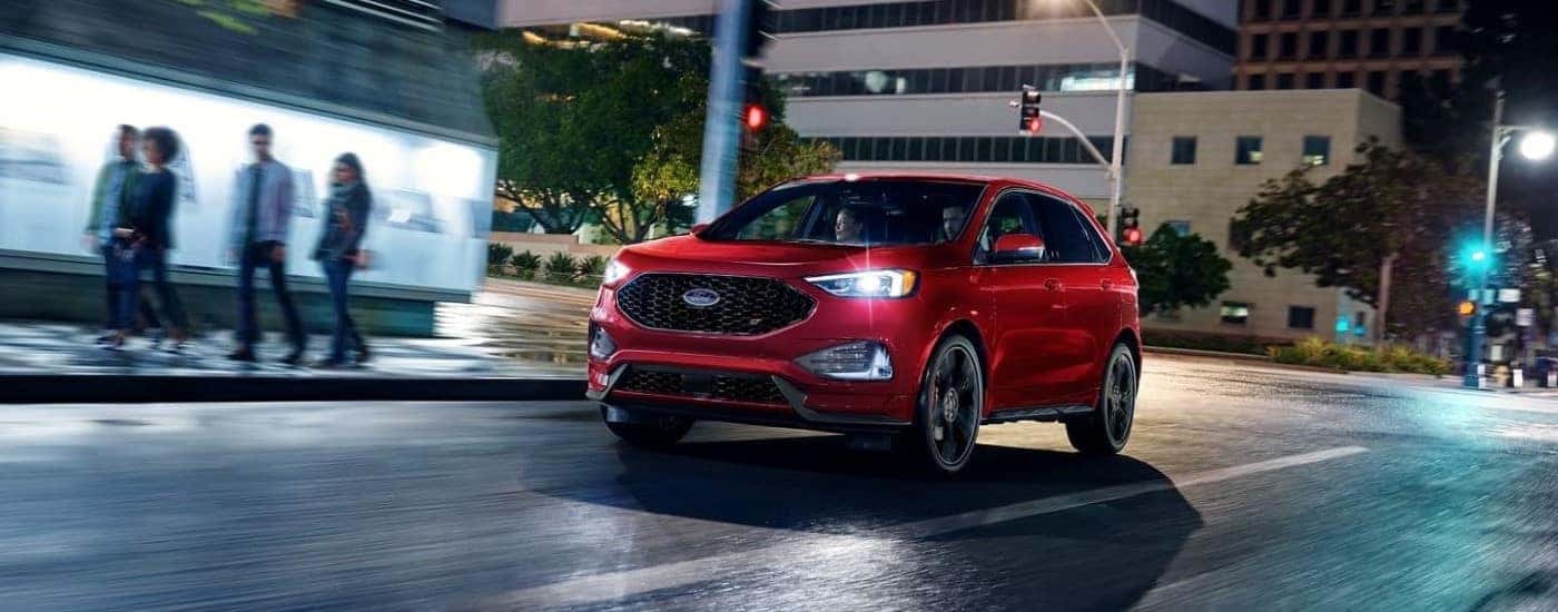 A red 2023 Ford Edge ST driving through a city after visiting a dealer with a used Ford for sale near Mechanicville.