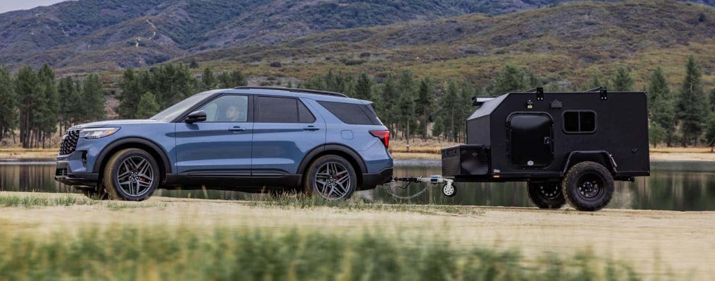 A blue 2025 Ford Explorer ST towing a camper near a lake.