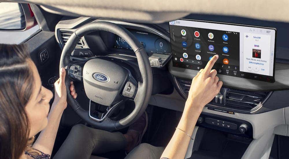 A woman using an infotainment display on a 2025 Ford Escape vs 2025 Toyota RAV4