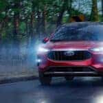 A red 2025 Ford Escape driving down a wet road at dusk