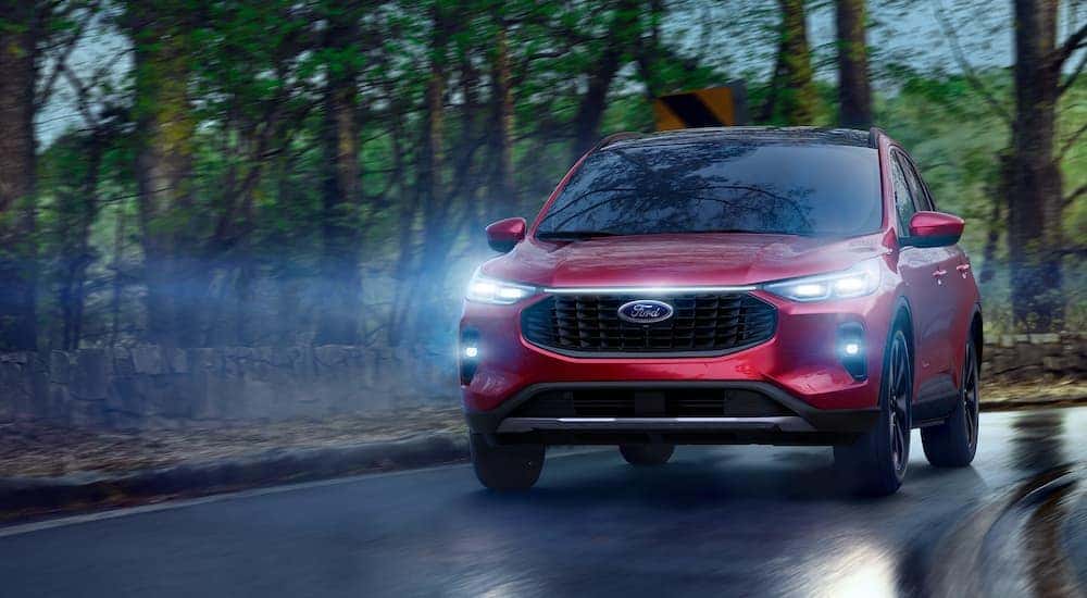 A red 2025 Ford Escape driving down a wet road at dusk