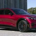 A red 2025 Ford Mustang Mach-E parked near a stone building.