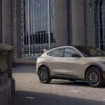 A tan 2025 Ford Mustang Mach-E Rally parked near a stone building.