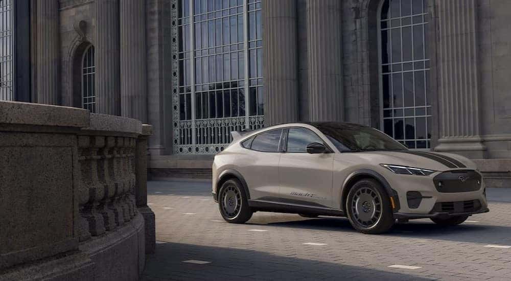 A tan 2025 Ford Mustang Mach-E Rally parked near a stone building.