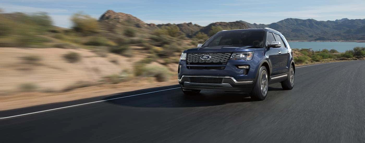 Dark blue 2018 Ford Explorer driving down an open road from a lake.