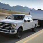 A white 2021 used Ford F-350 for sale towing a trailer on a highway.