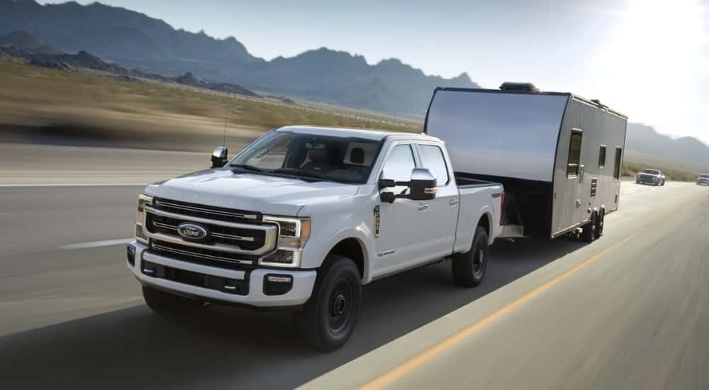 A white 2021 used Ford F-350 for sale towing a trailer on a highway.