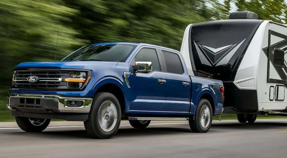 Blue 2025 Ford F-150 XLT towing a camper on a gravel road.