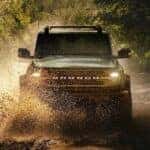 A green 2025 Ford Bronco off-roading in mud