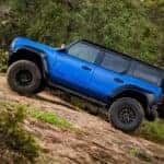 Side of a blue 2025 Ford Bronco Raptor off-roading on a rocky hill