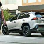 Woman walking from a white 2020 Toyota RAV4 Hybrid parked after visiting a dealer with used cars for sale near Colonie.