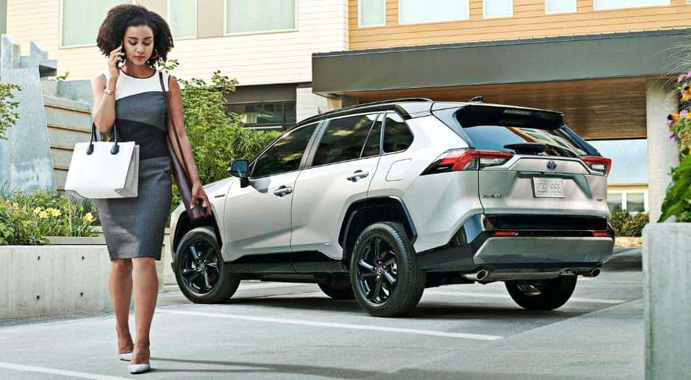 Woman walking from a white 2020 Toyota RAV4 Hybrid parked after visiting a dealer with used cars for sale near Colonie.