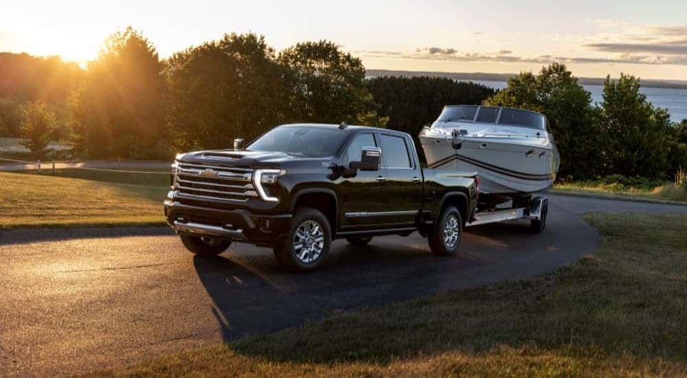A black 2024 Chevy Silverado 2500 HIgh Country towing a boat after viewing used trucks for sale near Latham.
