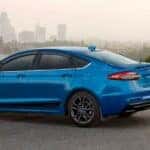 A blue 2020 Ford Fusion parked near two hikers.