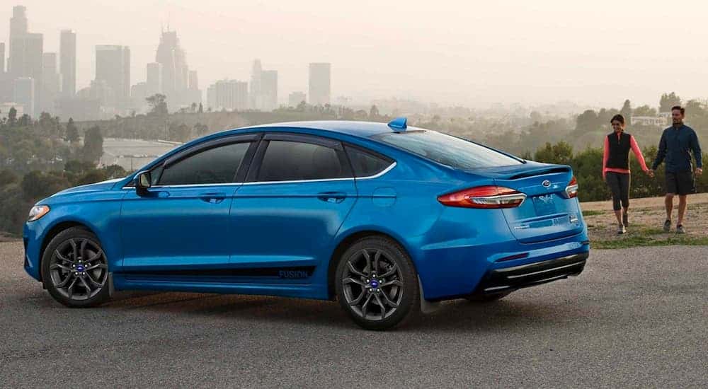 A blue 2020 Ford Fusion parked near two hikers.