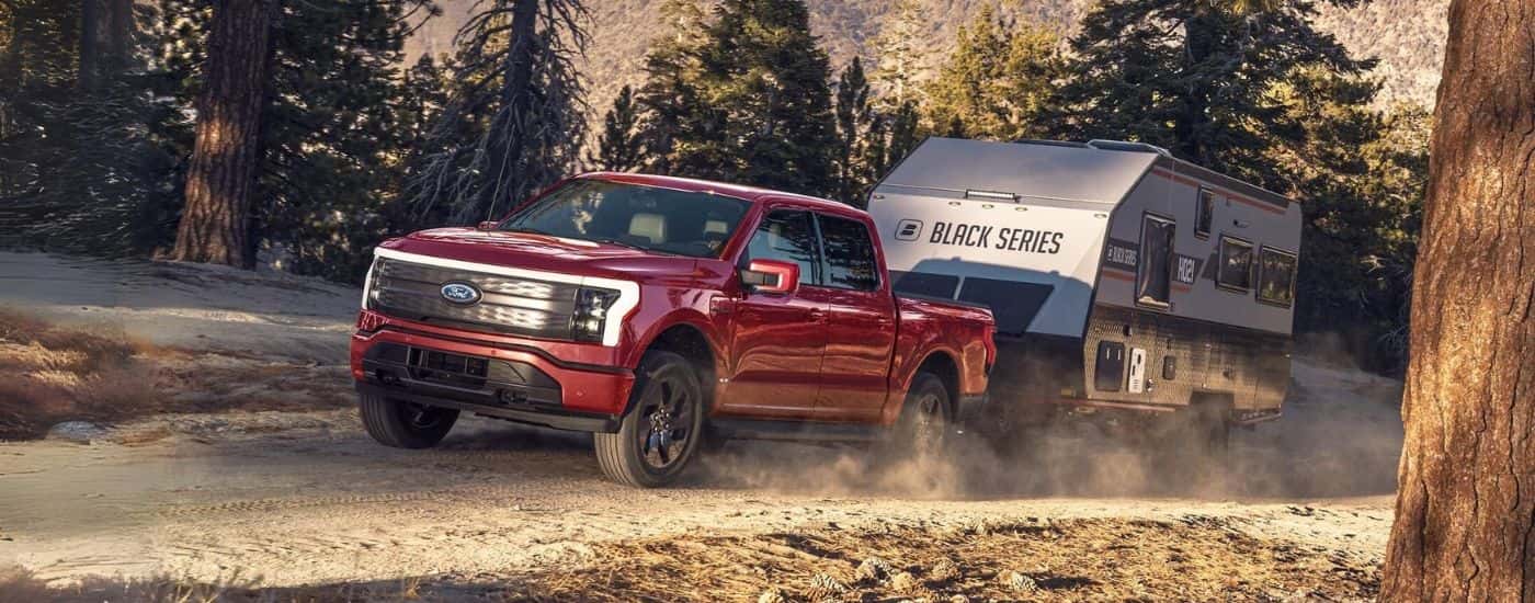 A red 2025 Ford F-150 Lightning towing a camper